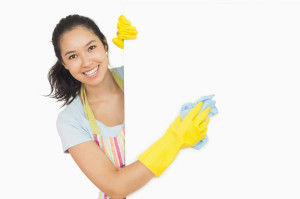 Cheerful woman cleaning white surface in apron and rubber gloves